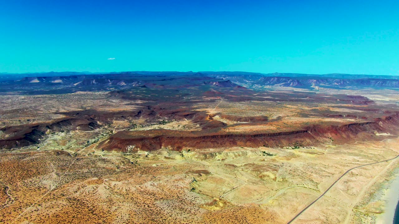 Aerial view of desert ridges and sandy flats under a blue sky.