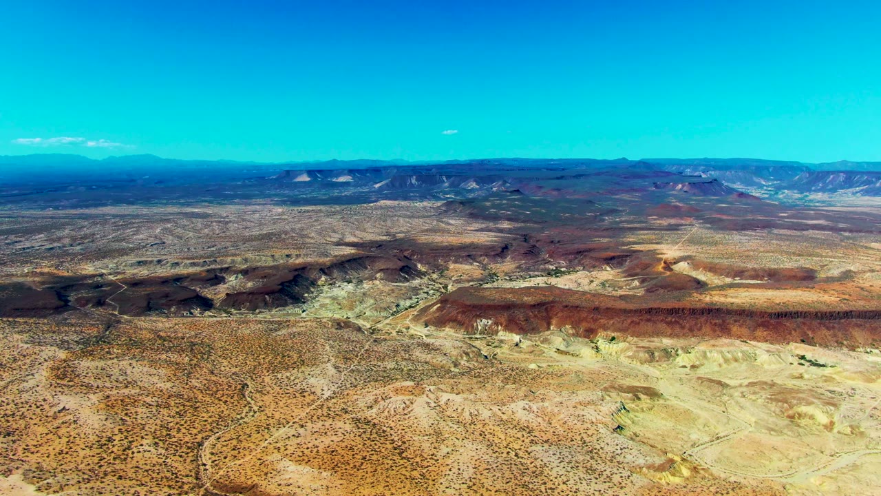 Third frame keeps the high San Juanico view on scrub-covered desert, red rock formations, distant blue ridges, and a small cloud slightly farther along the horizon with no visible people.
