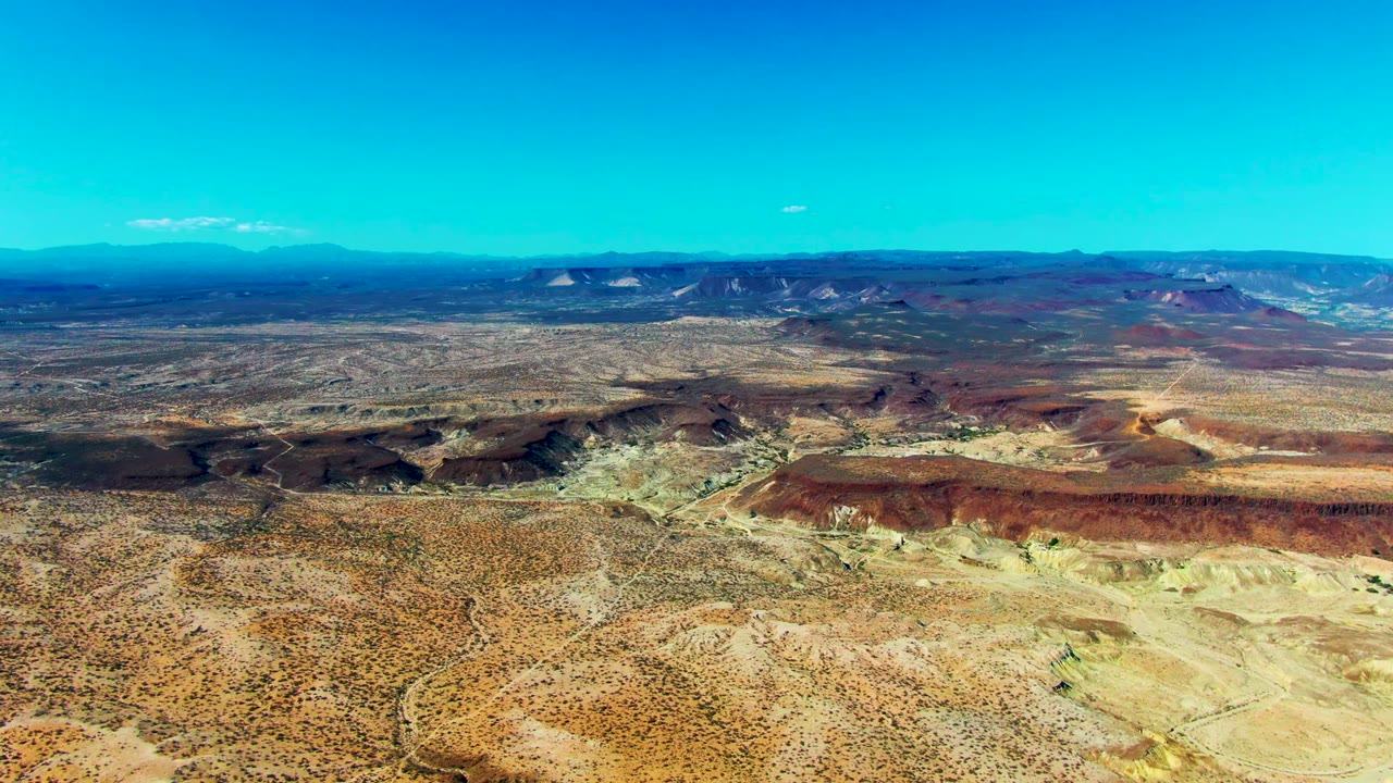 Wide opening view over San Juanico, Baja California Sur desert canyons, with sandy foreground, red-brown ridges, distant mountains, and no visible people.
