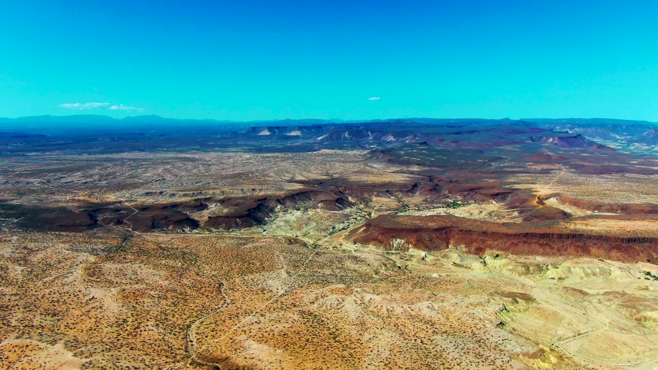 Aerial desert plateau with rocky ridges and distant mountains.