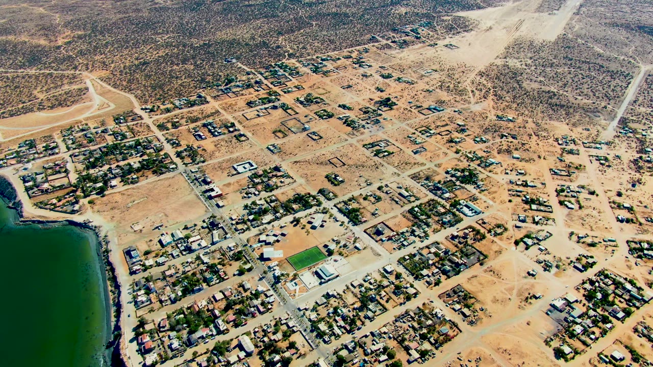 Aerial desert town grid with roads, houses, and water on the left.