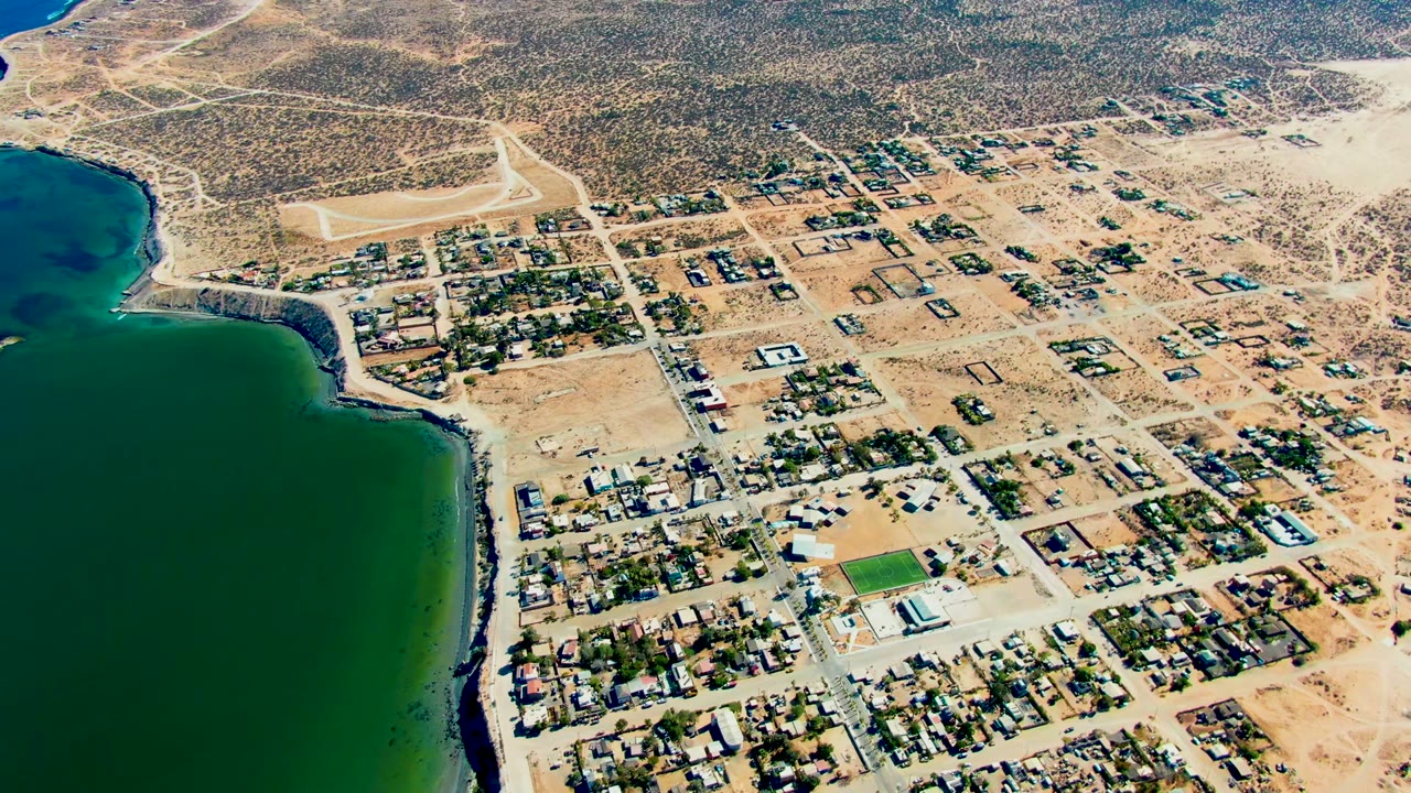 Coastal residential blocks and sandy roads beside calm bay water.
