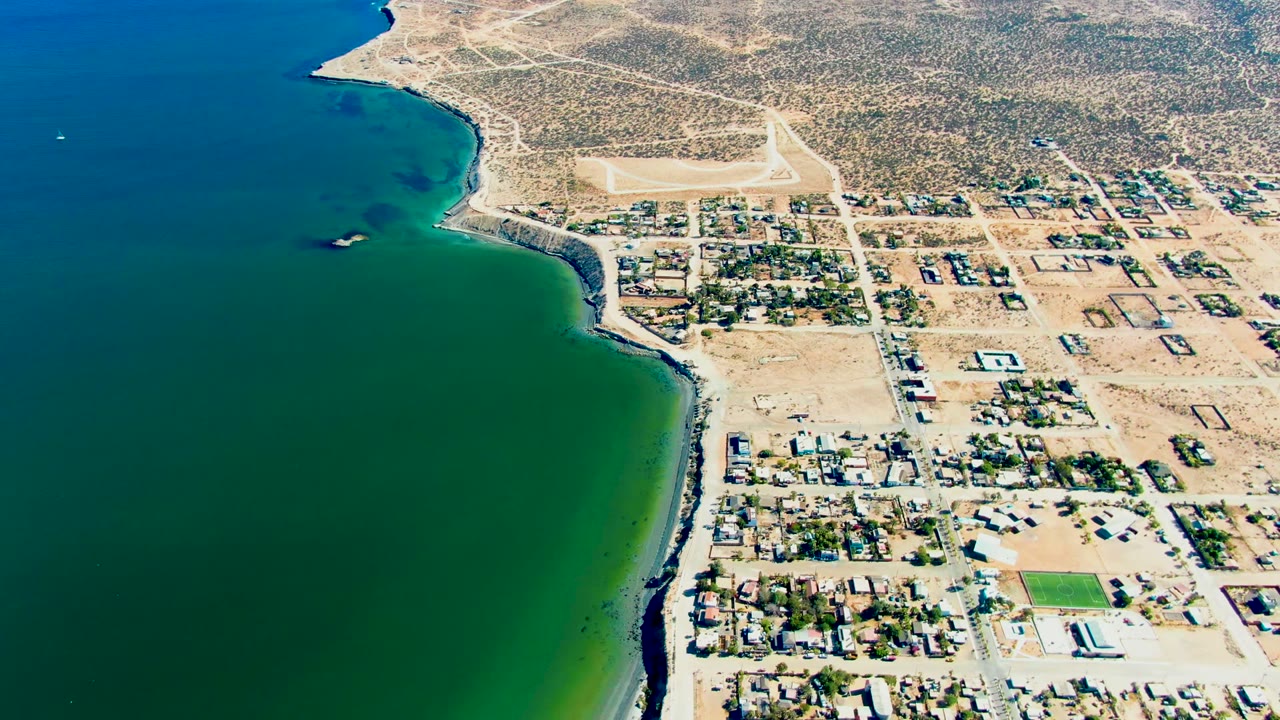 Aerial coastline view with ocean on the left and a small coastal town on the right.