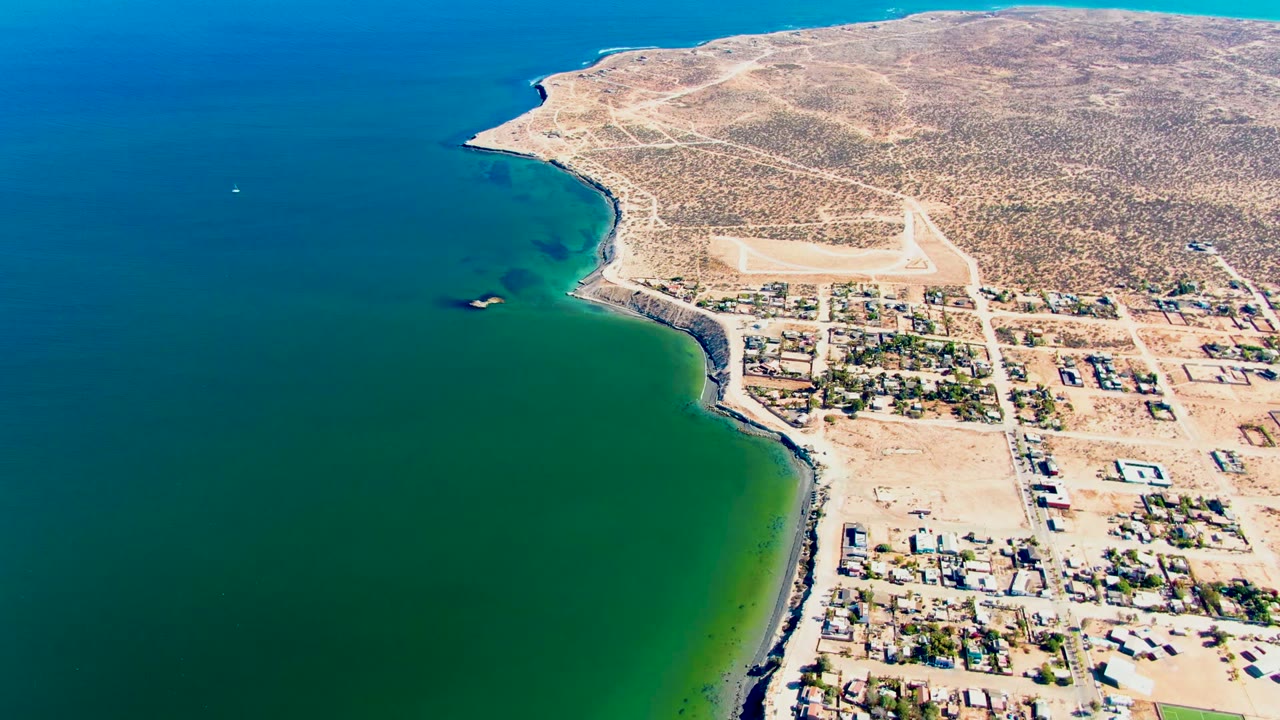 Coastal town and curved shoreline seen from above with a small boat on the water.