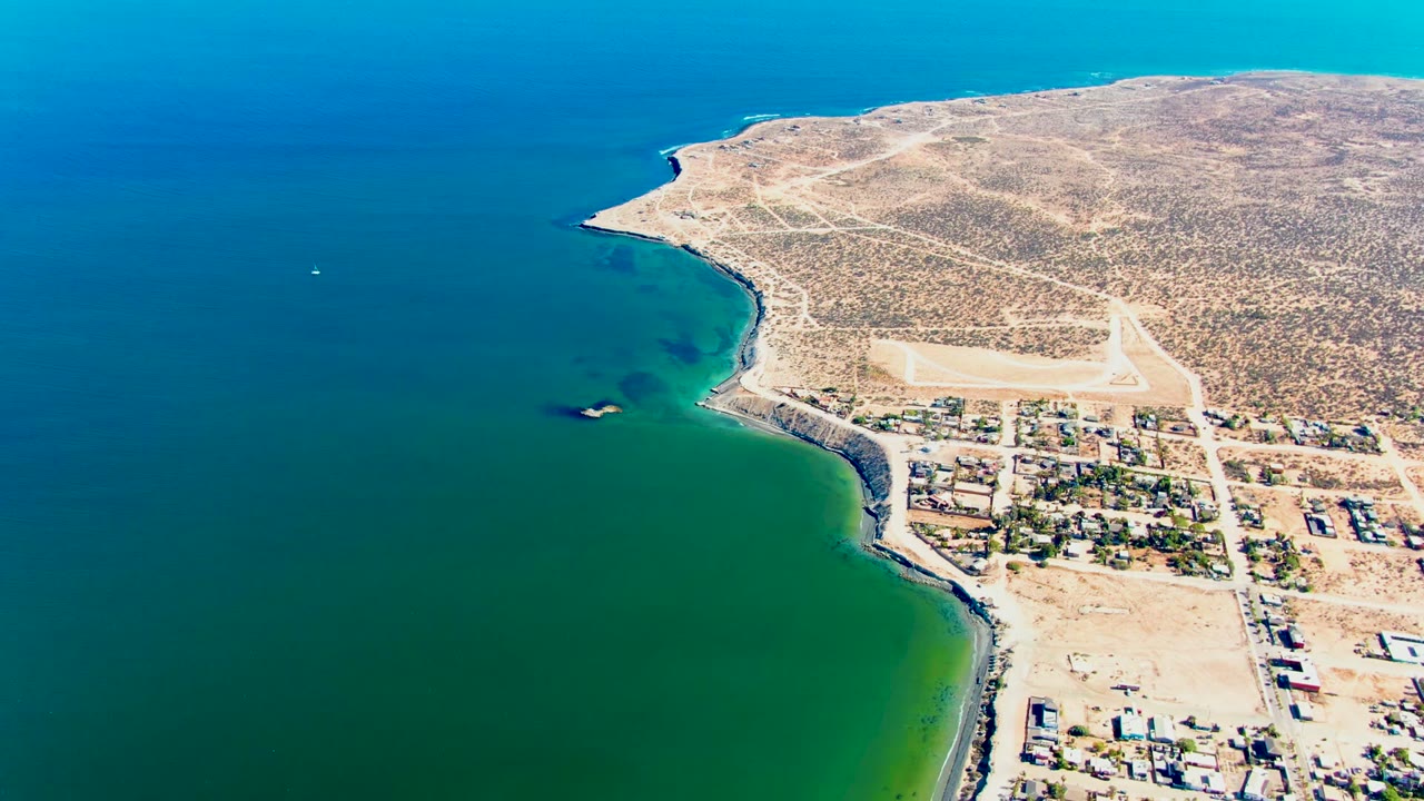 Third frame from the San Juanico aerial places the settlement farther right, with calm water dominating the left half and desert roads crossing the upper shoreline, with no visible people.