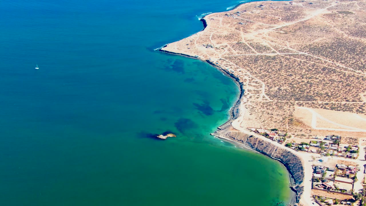 High aerial of curved shoreline, clear water, roads, and clustered buildings.