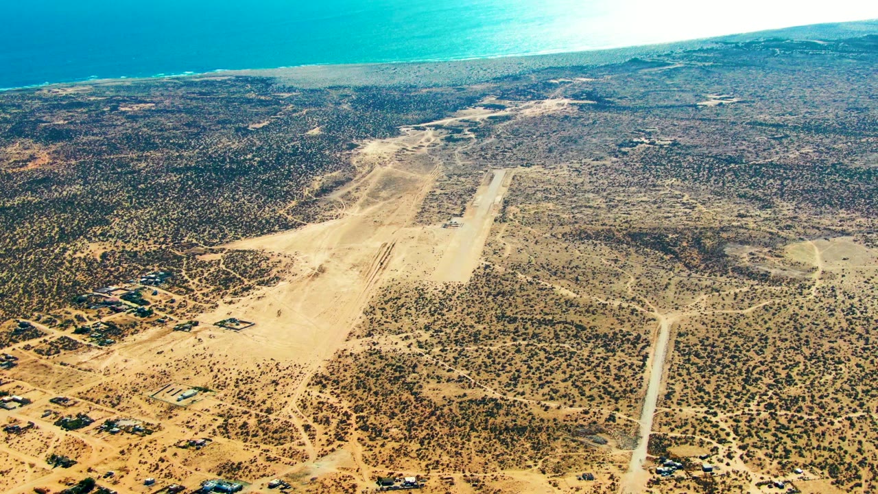 Aerial desert runway with sparse buildings and bright coastline.
