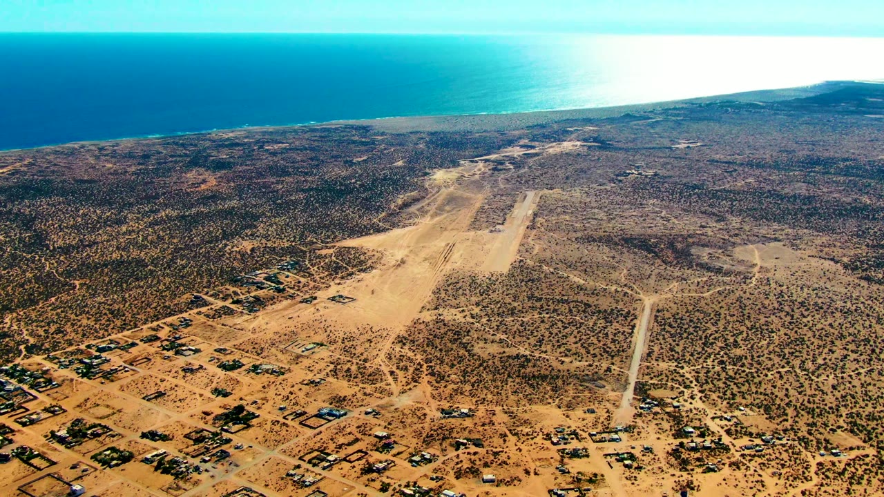 Drone view of coastal airfield surrounded by arid scrub and dirt roads.