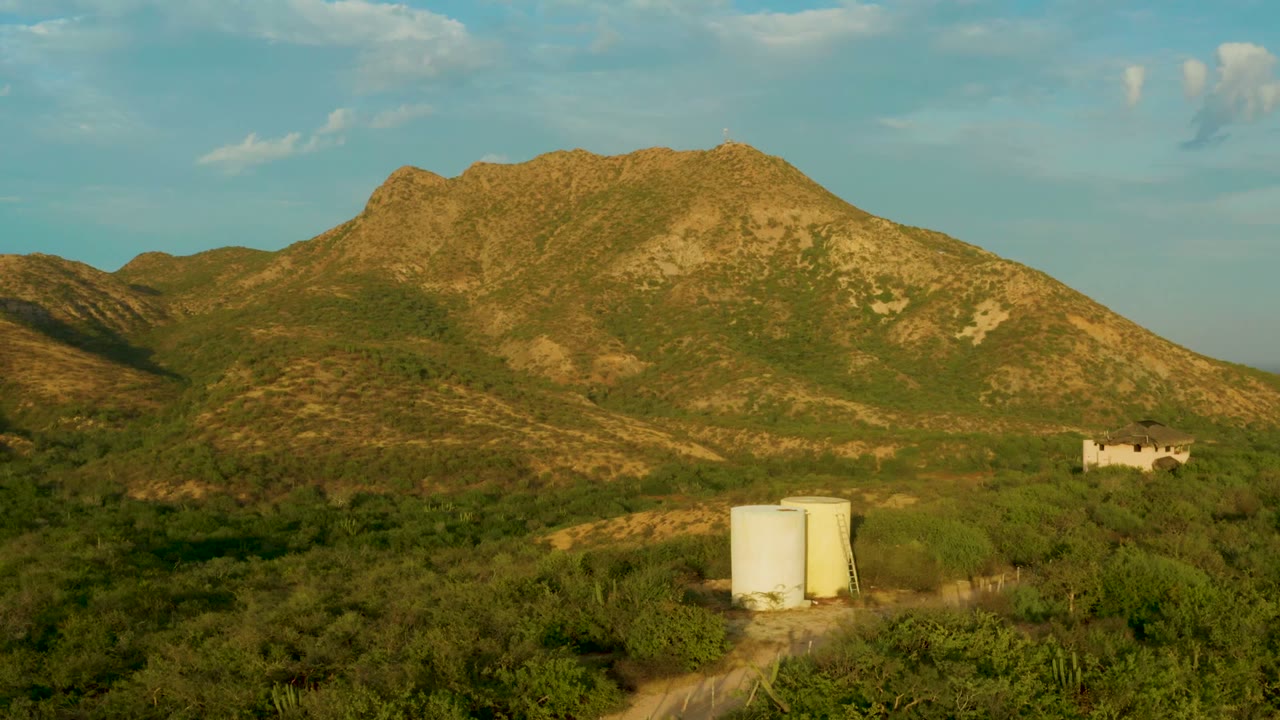 Aerial view of scrubland, white tanks, dirt track, and mountain ridge.