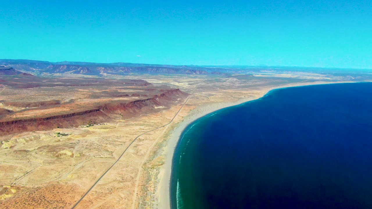 High aerial coastline with desert road, beach, ocean, and mountains.