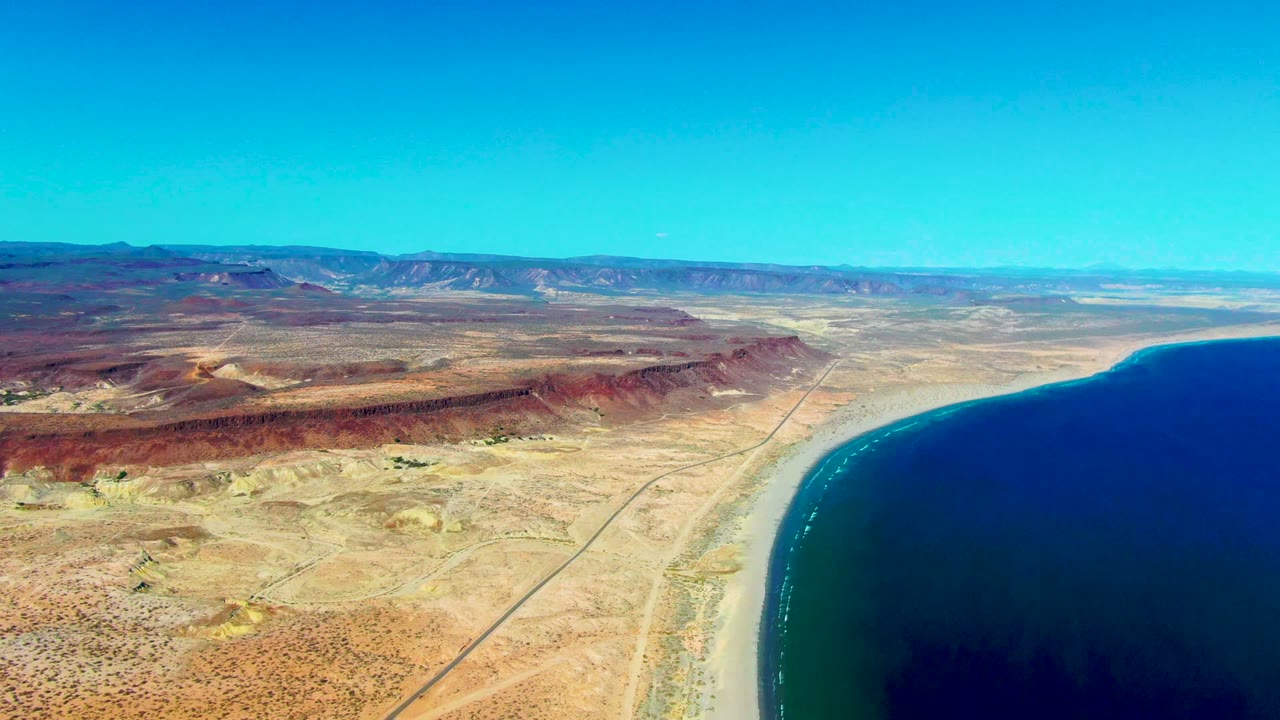 Wide coastal desert aerial with curved beach and inland road