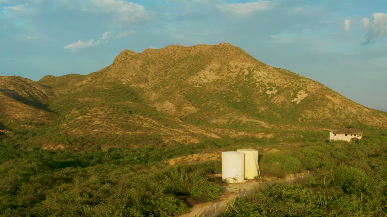 Green hillside landscape with white tank, dirt track, and small distant structure.