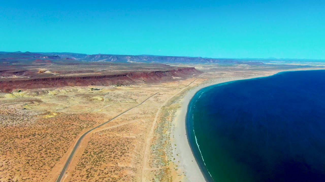 Coastal desert and road running near a sandy shoreline with ocean to the right.
