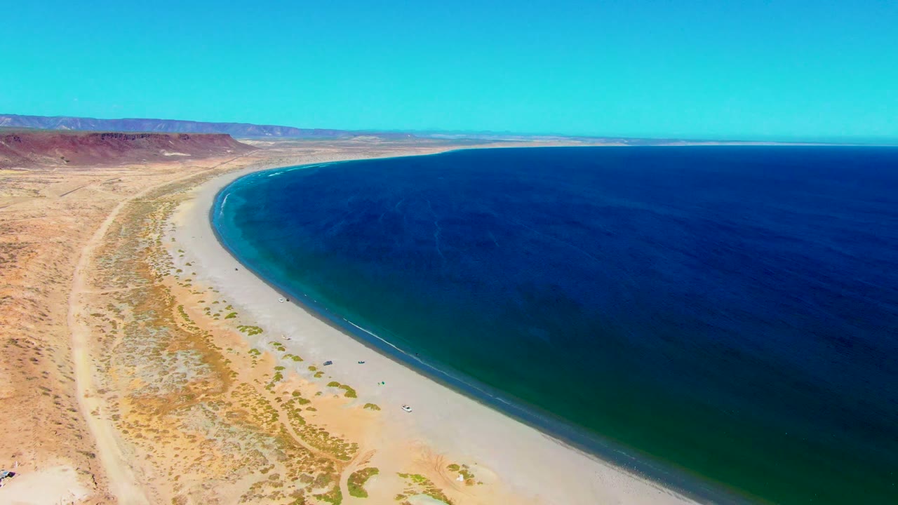 High aerial coastline view with desert tracks, sandy beach, and blue water.