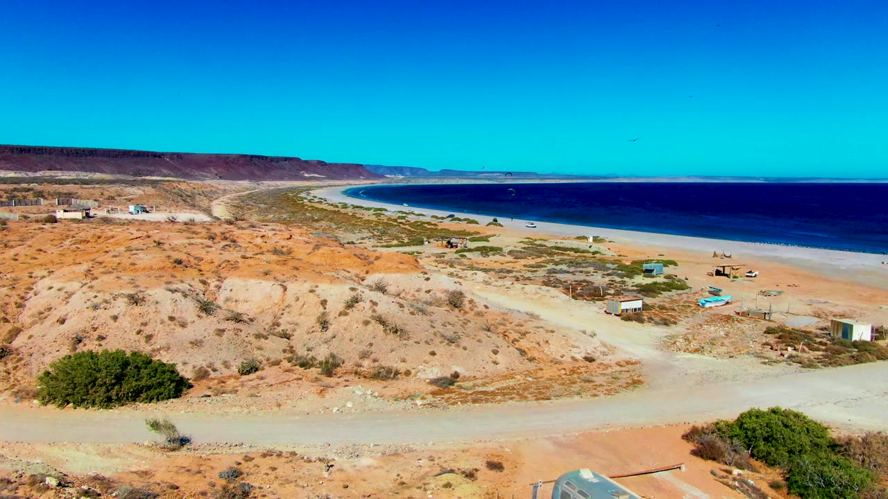 Coastal campsite terrain with dirt road, small structures, beach, and blue ocean.