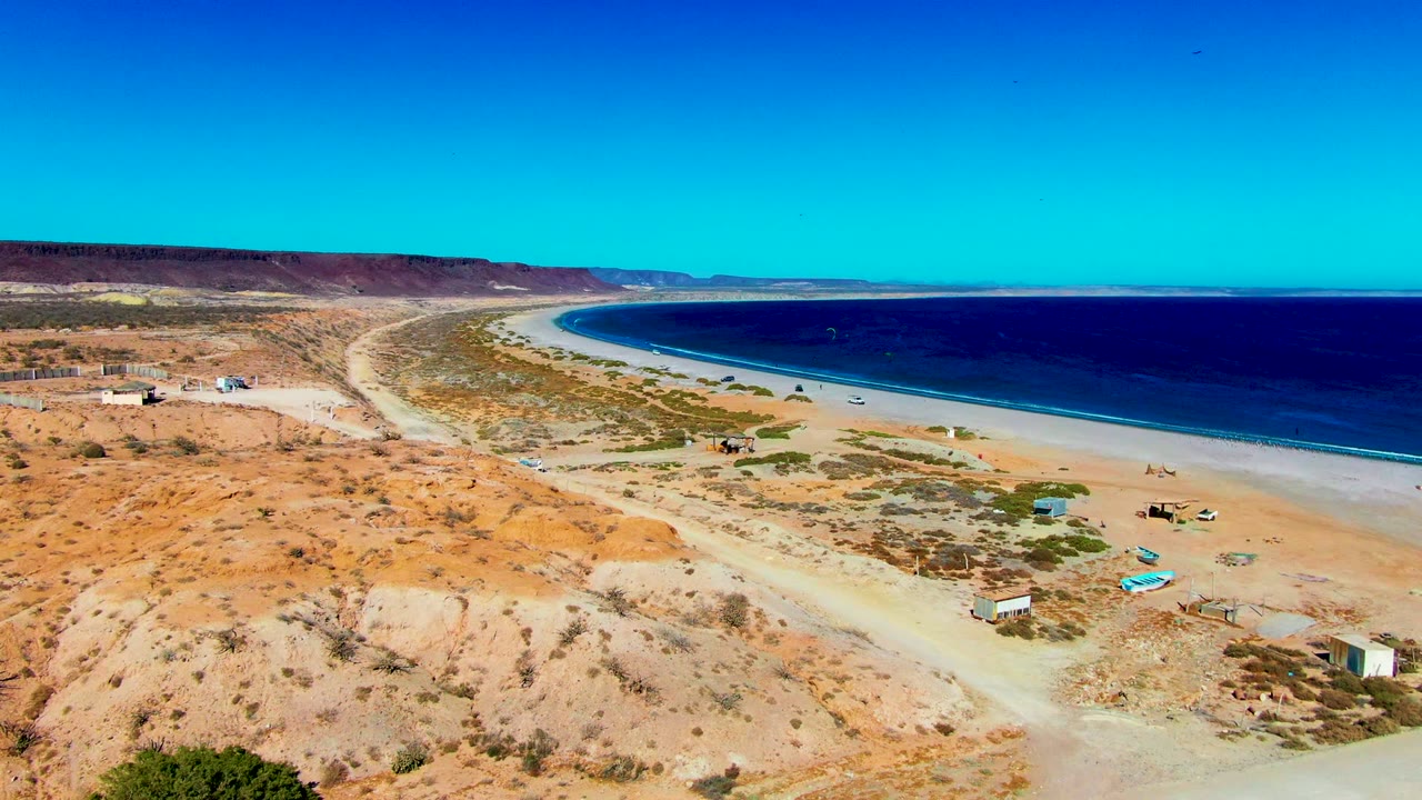 Wide drone view of desert slope, curved coastline, beach, and ocean.