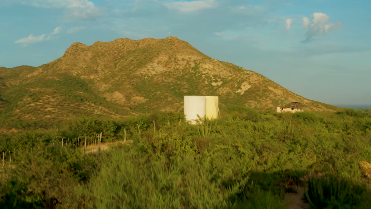 White tanks in green vegetation below a rocky hillside and blue sky