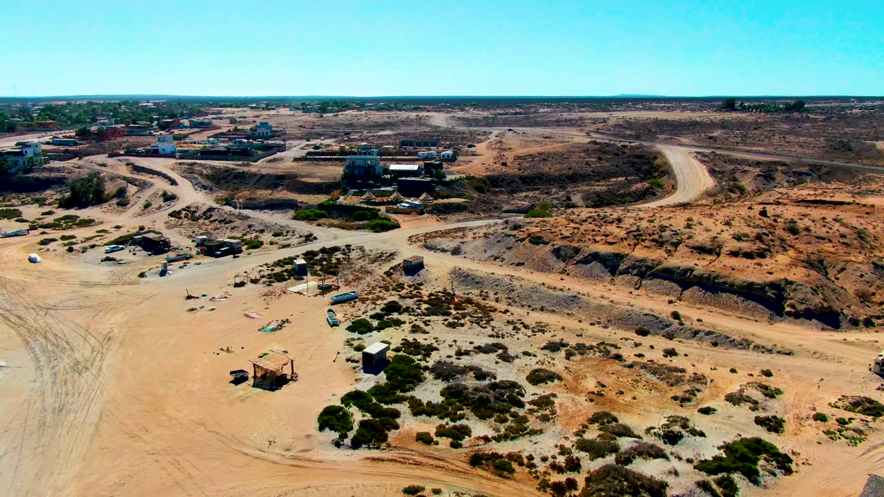 Opening aerial frame over San Juanico, Baja California Sur showing sandy dirt roads, low desert scrub, scattered small structures, distant buildings, and no visible people.