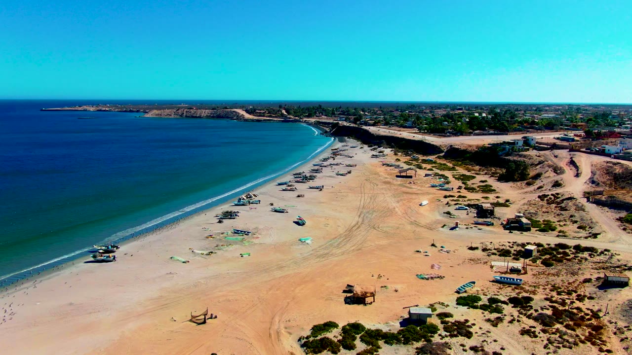 Wide aerial coastline with boats on sand near calm blue water.