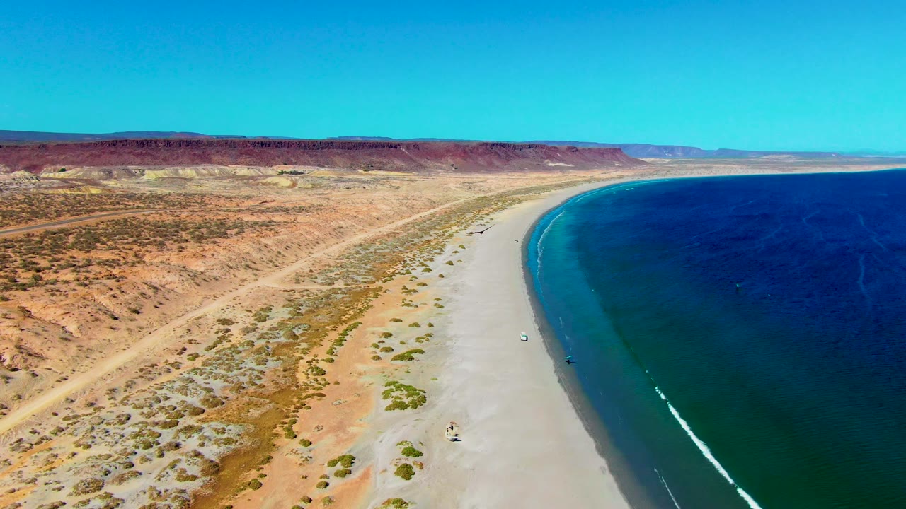 Curving sandy shoreline beside deep blue water and arid hills.
