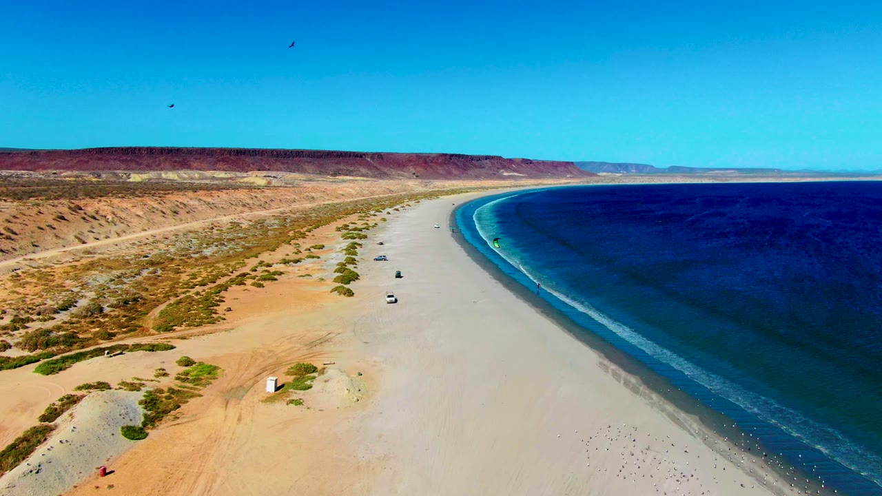 High aerial beach view with vehicles spaced along the sand and waves at right.