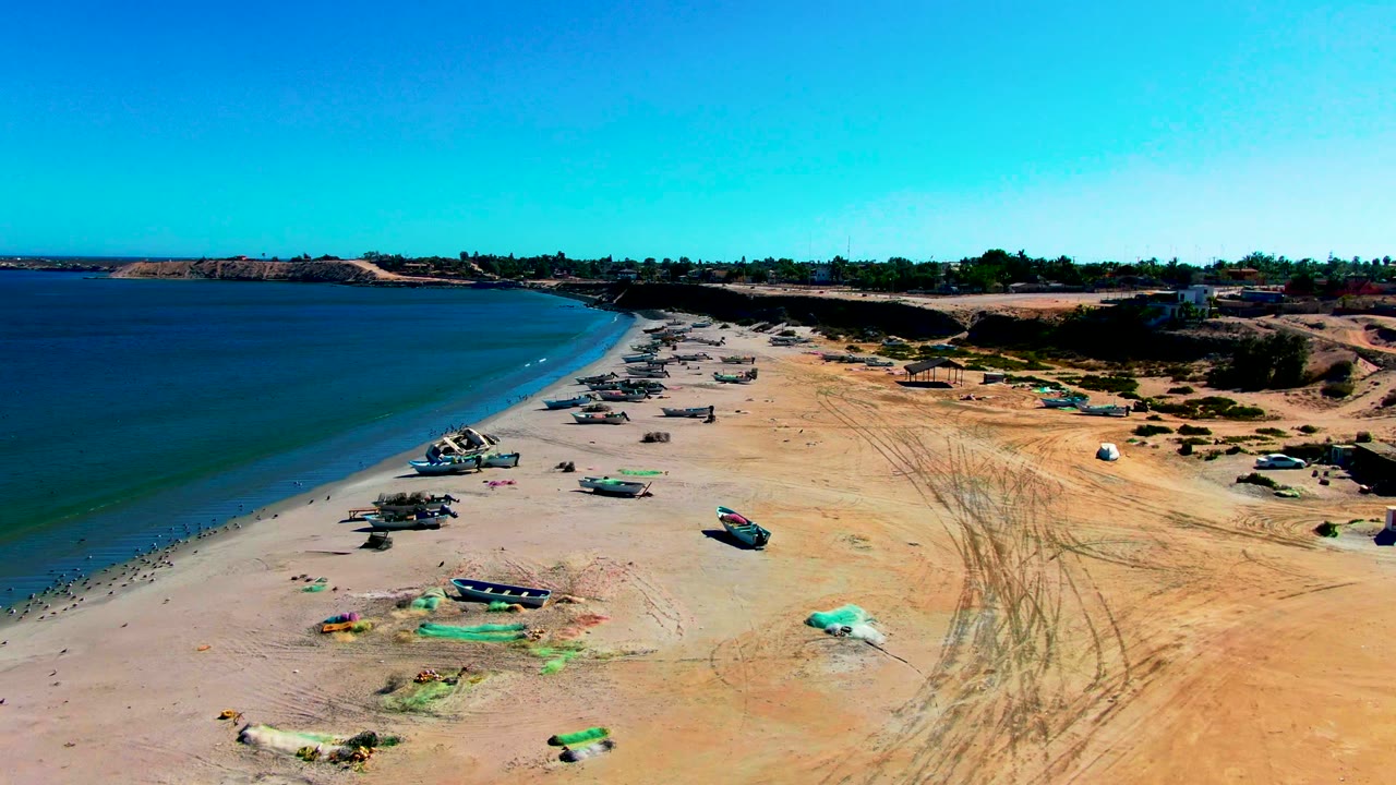 Fishing boats and nets line a sandy shoreline under a clear blue sky.
