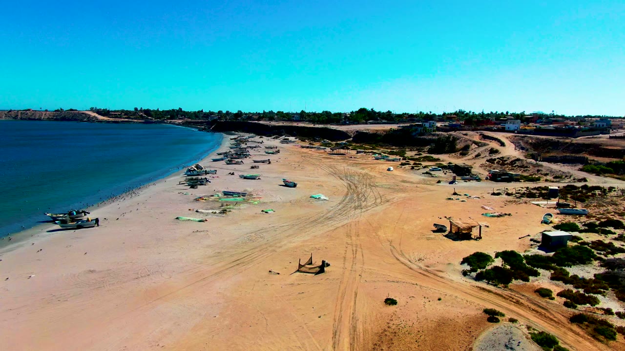 Fishing boats and green tarps line a wide sandy shore near the ocean.