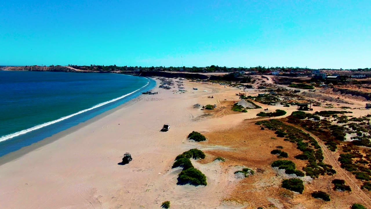Drone view of a lone 4x4 moving along open beach near the surf.