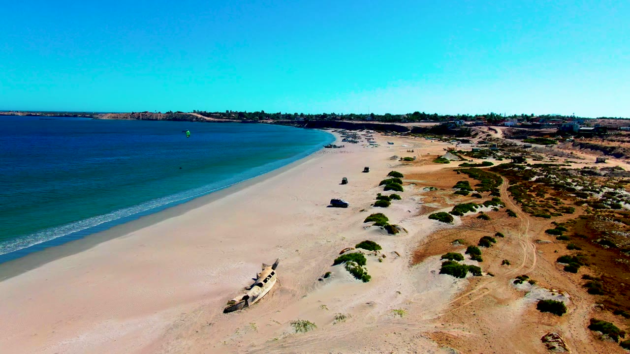 High coastal view with ocean, pale sand, shrubs, and tire tracks