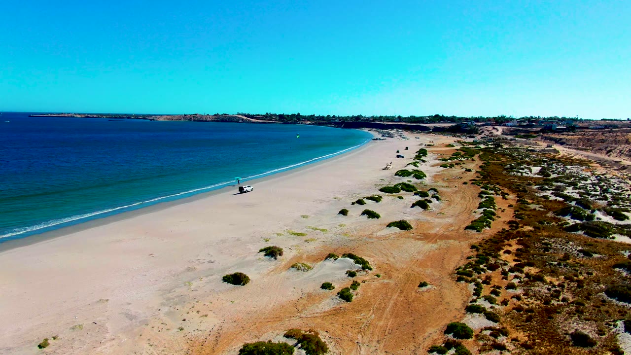 White 4x4 traveling along a broad sandy shoreline with dunes inland.