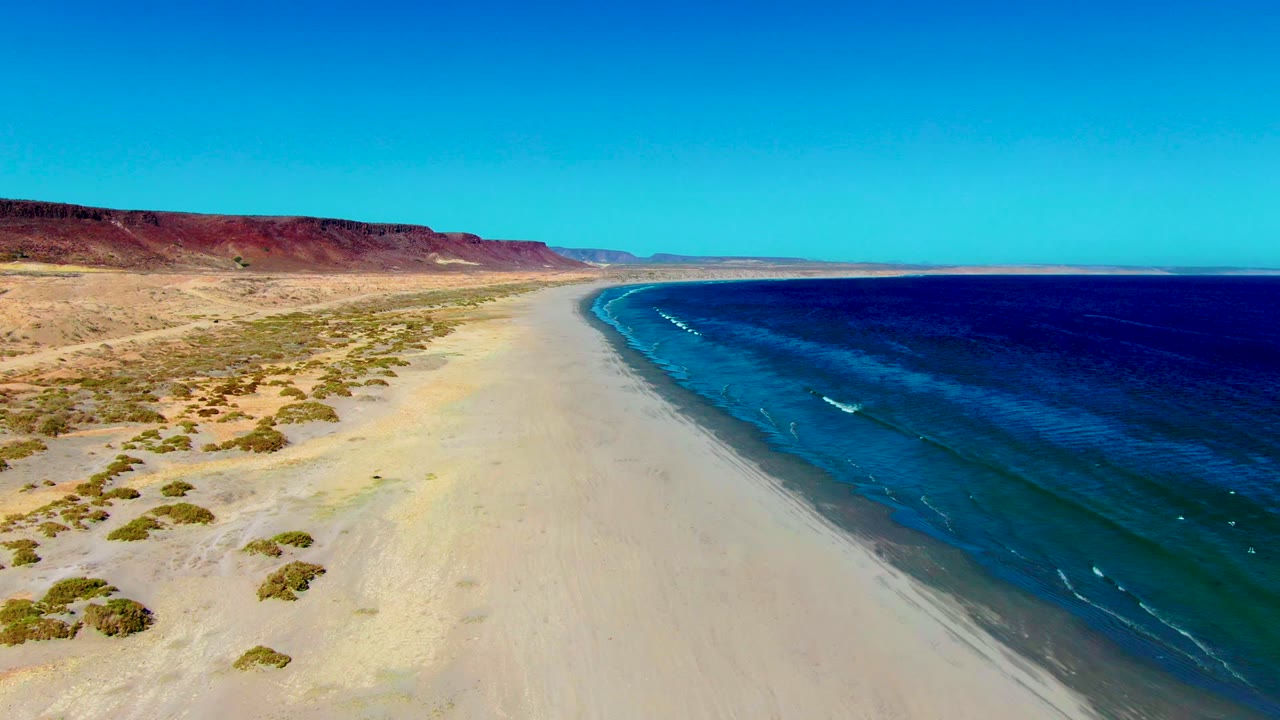 Wide beach and ocean shoreline with small whitecaps near the sand.
