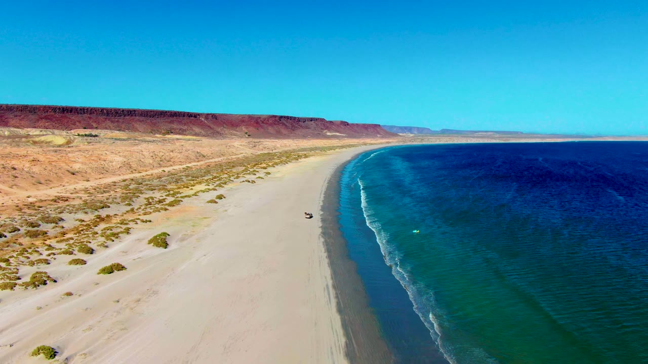 Vehicle moving along the sand near a curving shoreline.