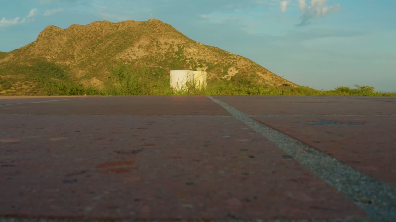 Asphalt foreground with diagonal road line and mountain beyond shrubs
