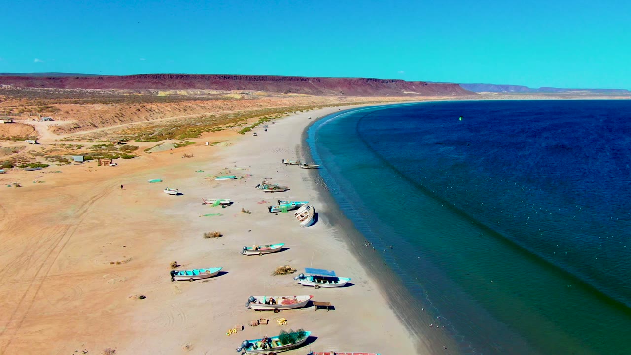 Boats rest on a wide sandy shoreline with deep blue water to the right.