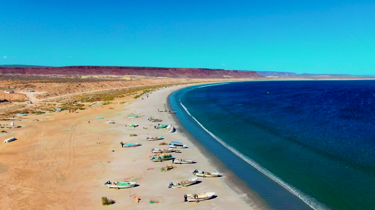 Fishing boats line a sandy beach with ocean surf along the right side.