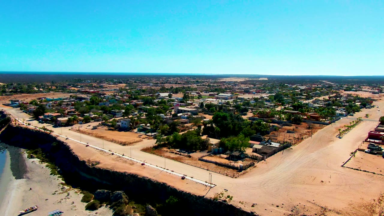 Drone view of beach access road beside water and low buildings.