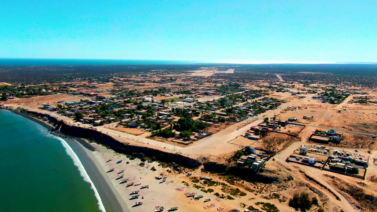 Aerial coastline with sandy beach, boats, roads, and village buildings