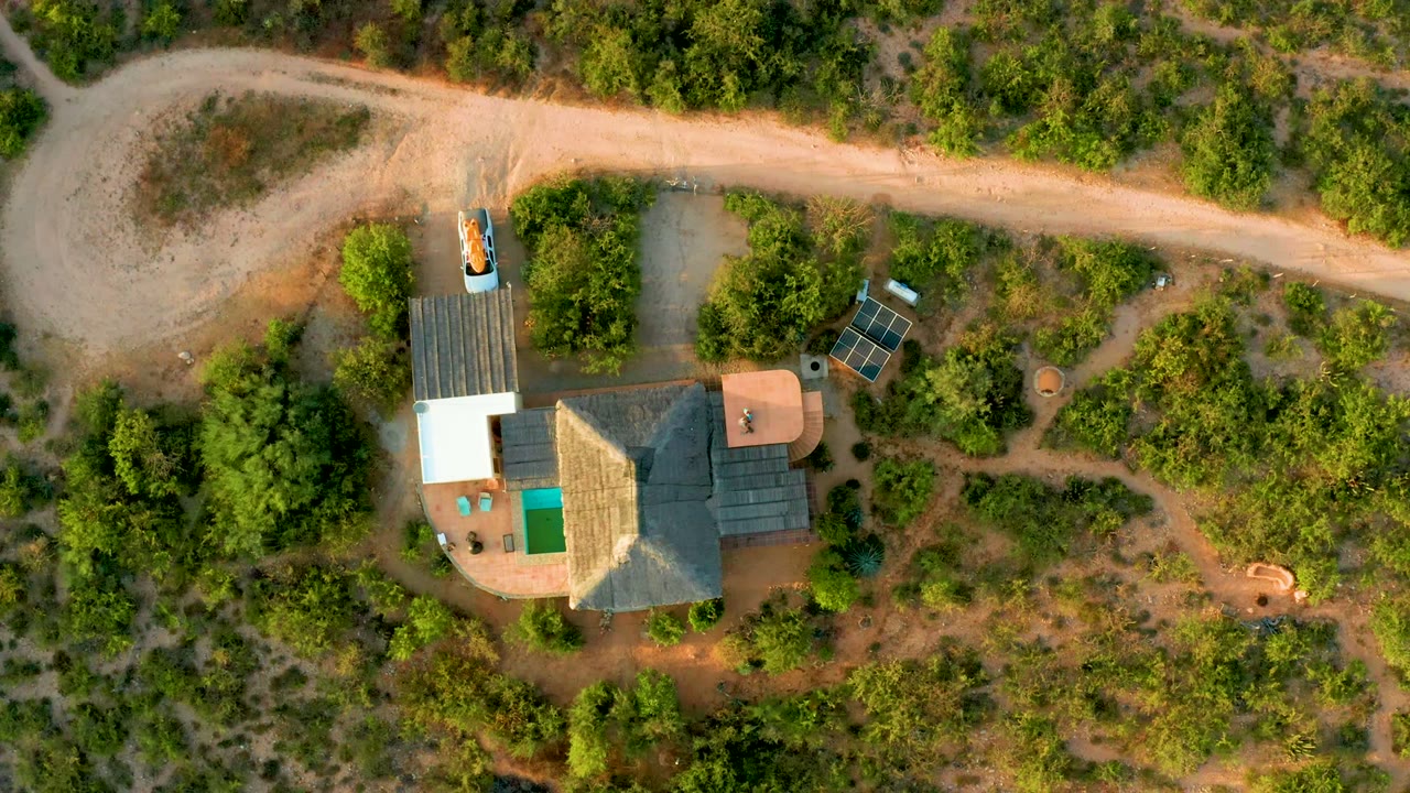 Aerial view of a house compound with solar panels near an unpaved road.