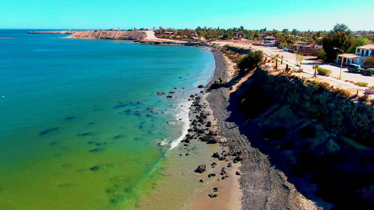 Elevated coastal view with turquoise water, rocks, beach, cliff, and road.