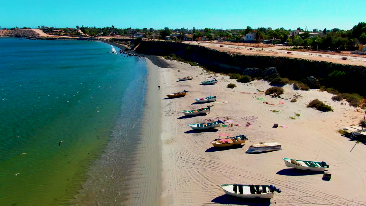 Small boats line a sandy shore with clear water on the left.