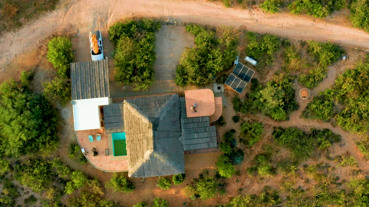 Aerial view of a car moving along a dirt road above a rural house.