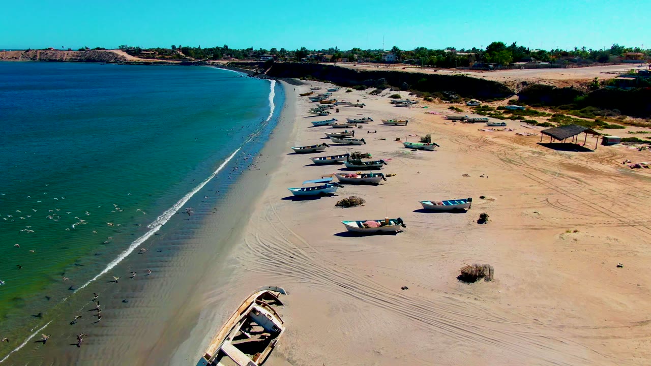 Fishing boats scattered along a sandy shoreline with waves rolling in.