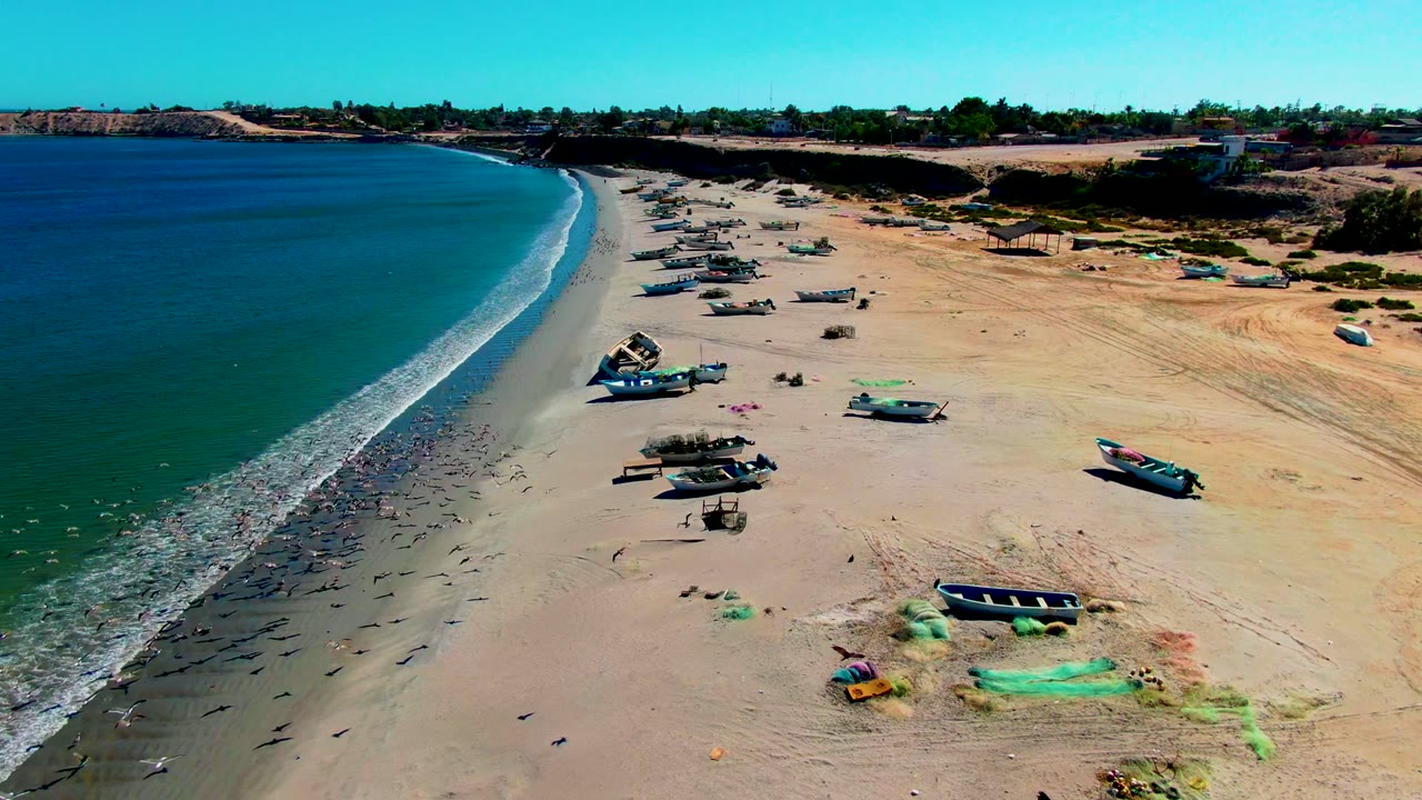 Fishing boats sit on open sand as waves trace the beach edge.