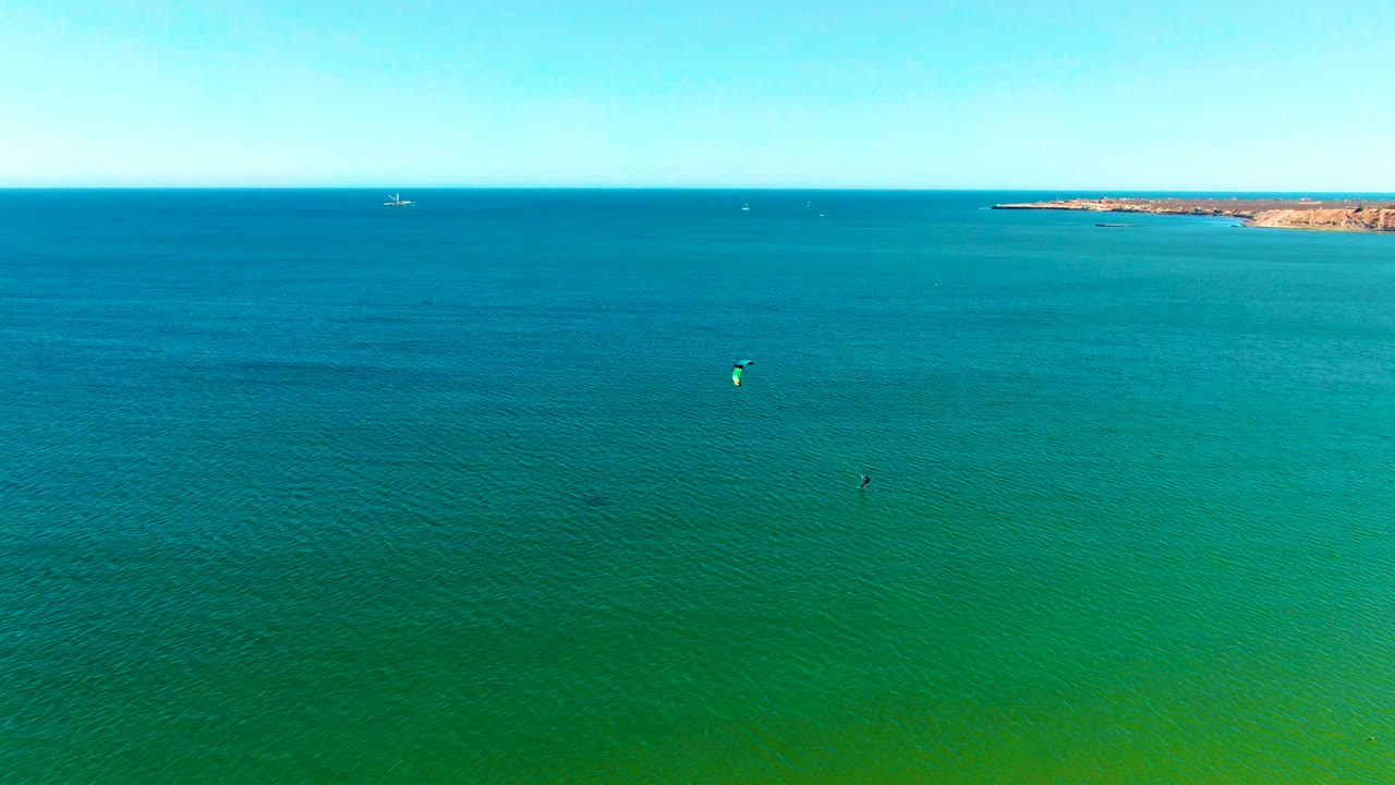 Turquoise ocean surface with distant coastline and a small kite canopy over the water.