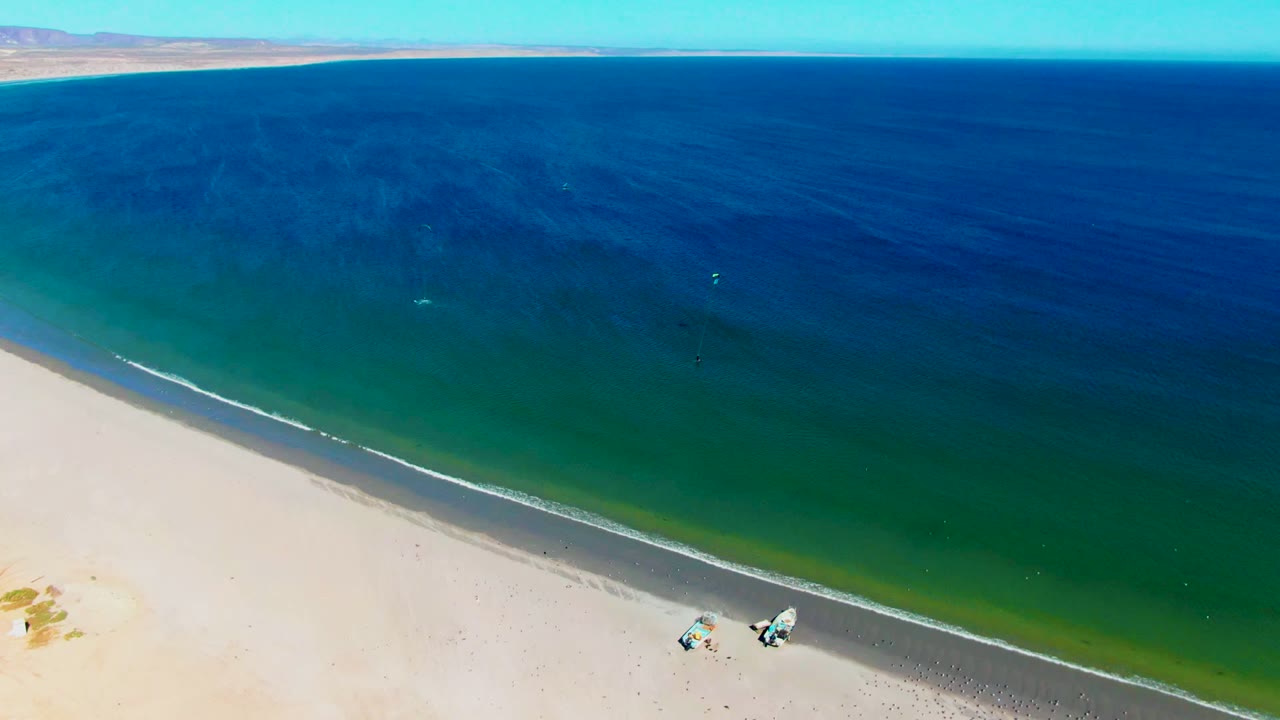Aerial San Juanico beach view with the shoreline running diagonally, green shallows near the sand, deeper blue water beyond, and no identifiable people visible.