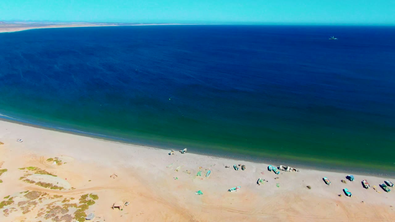 High aerial shoreline with boats on sand and dark blue ocean beyond.