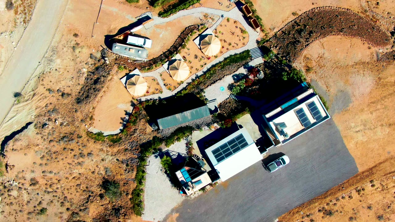 Aerial view of solar-roofed buildings beside sandy road and circular shade areas.