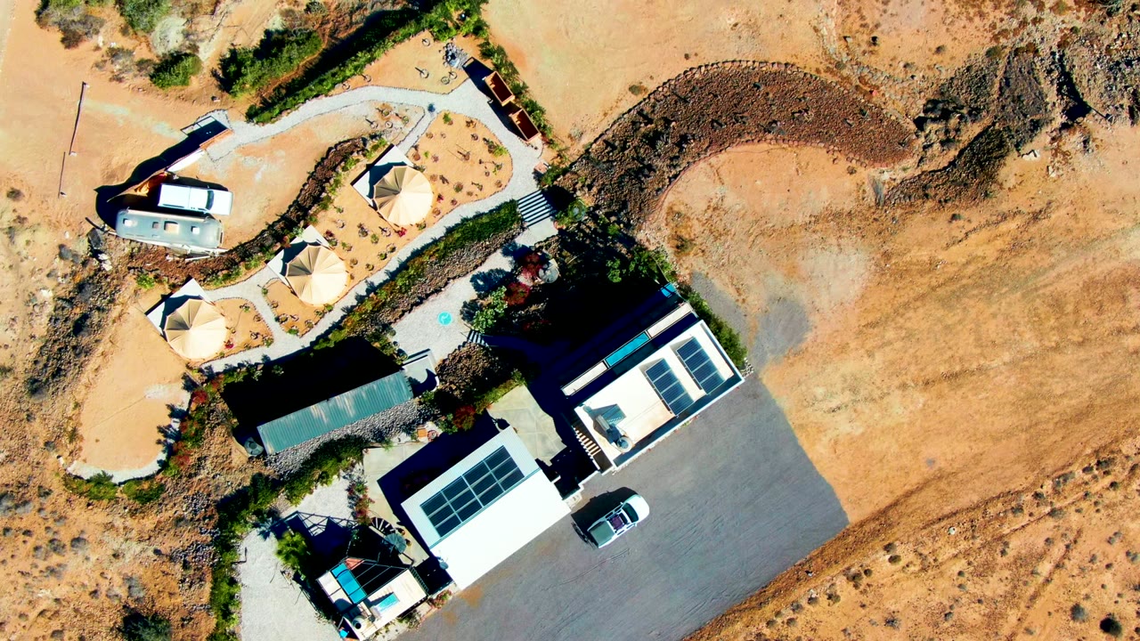 Aerial view of solar-roof buildings, shade domes, and desert road.