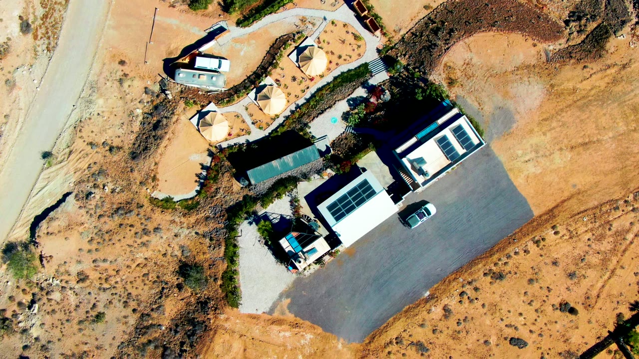 Aerial view of sandy property with structures, solar panels, and a paved lot.