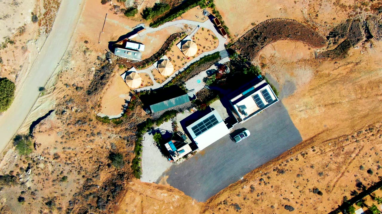 Aerial view of desert road, low buildings, paved lot, and sparse shrubs.
